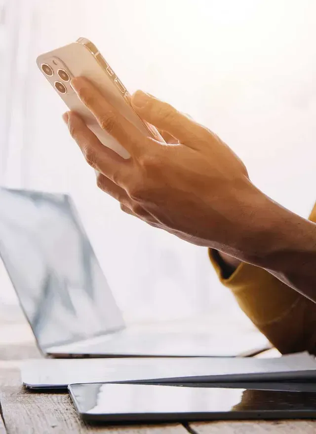 Una persona está sentada en una mesa usando un teléfono celular.