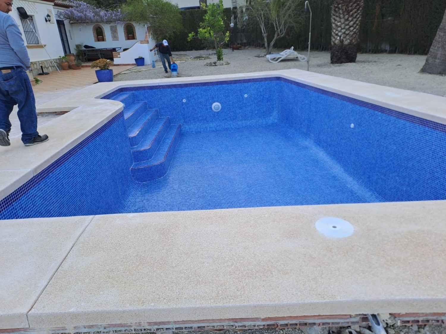 Escalera de piscina junto al agua turquesa y terraza de piedra con rejilla de desagüe.