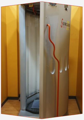 Una cabina de bronceado está ubicada en una habitación con paredes amarillas.