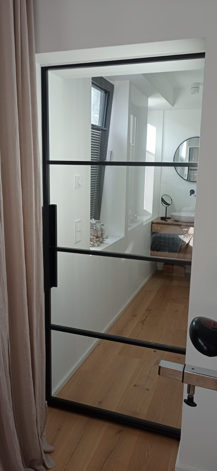 Eine Glastür mit schwarzem Rahmen führt zu einem Badezimmer.