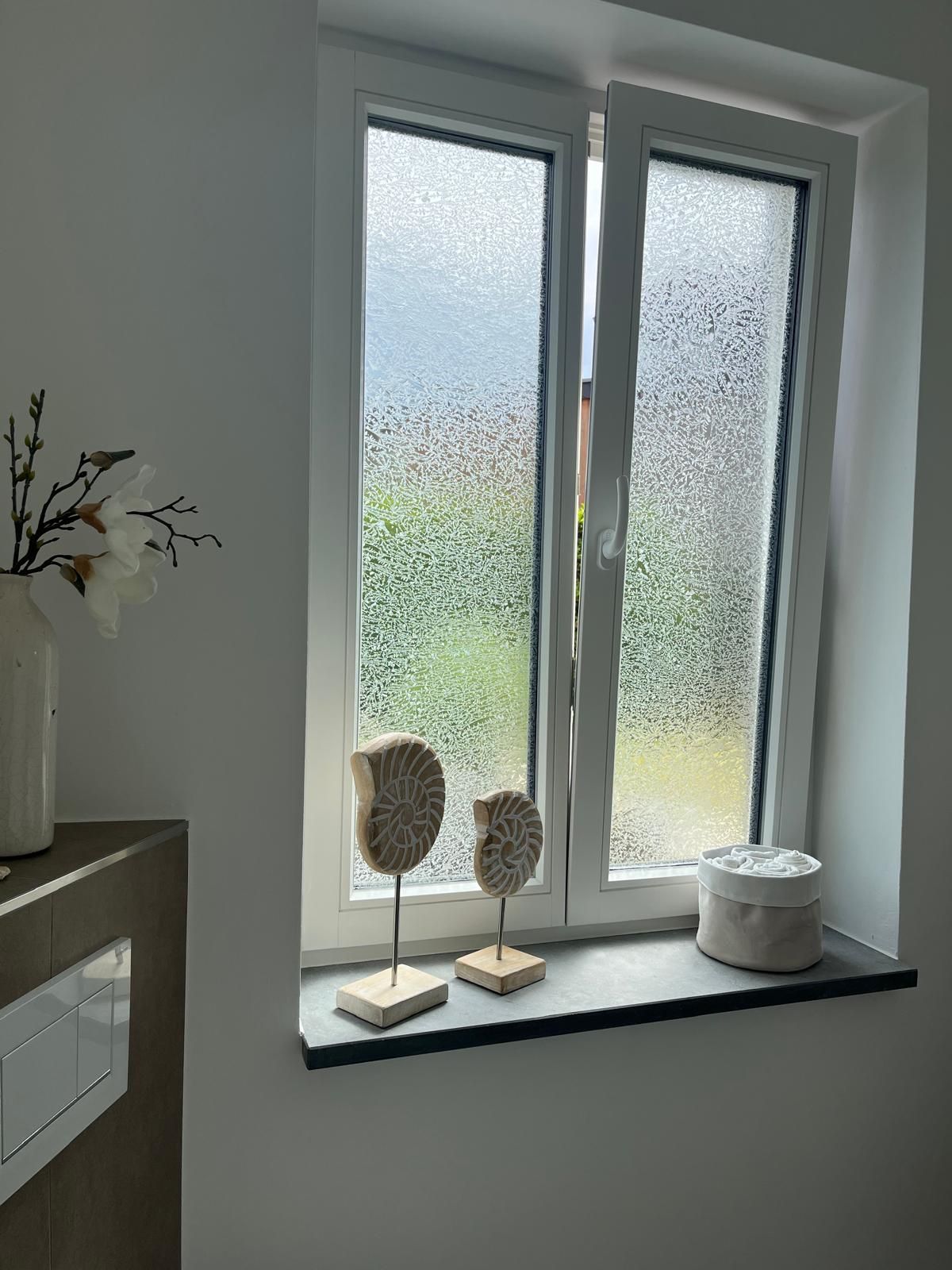 Zwei Skulpturen sitzen auf einem Fensterbrett neben einem Fenster.