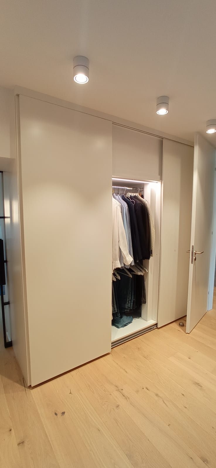 Ein begehbarer Kleiderschrank mit Schiebetüren und Holzboden.