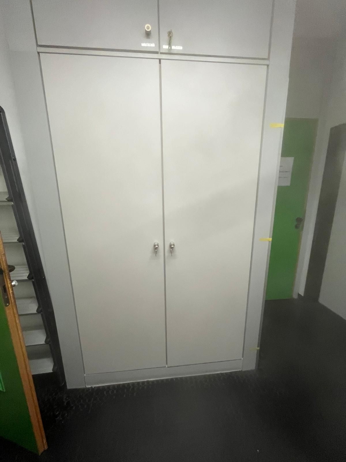 Ein weißer Schrank mit zwei Türen steht in einem Flur neben einer grünen Tür.