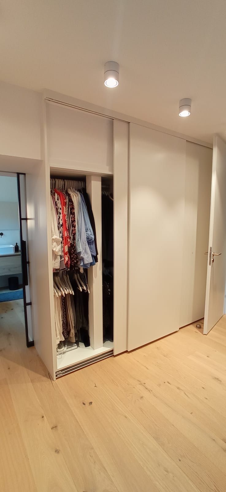 Ein Schrank mit vielen Klamotten darin und ein Holzboden.
