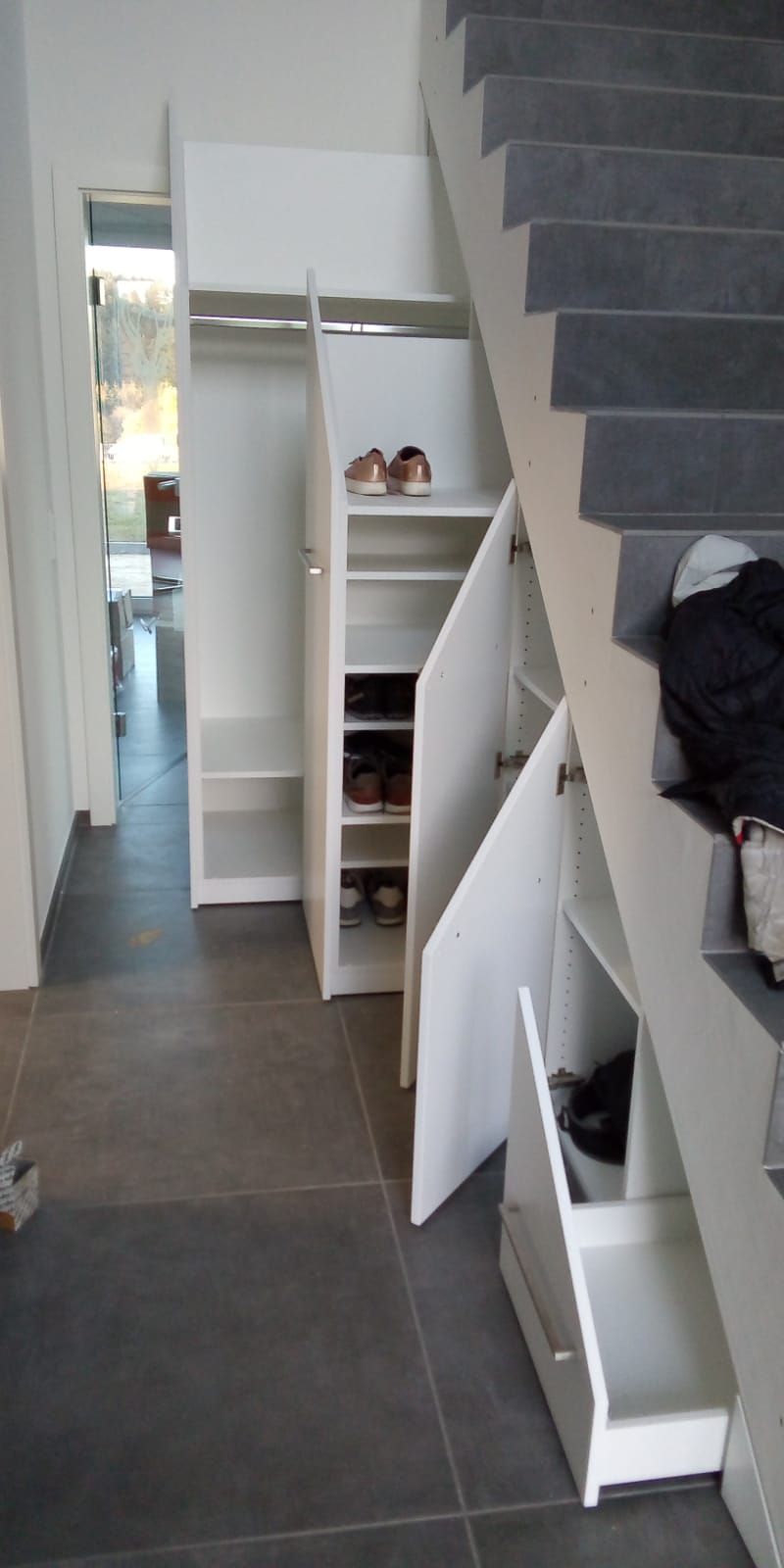 Unter der Treppe befindet sich ein Schrank mit Schubladen und Regalen.