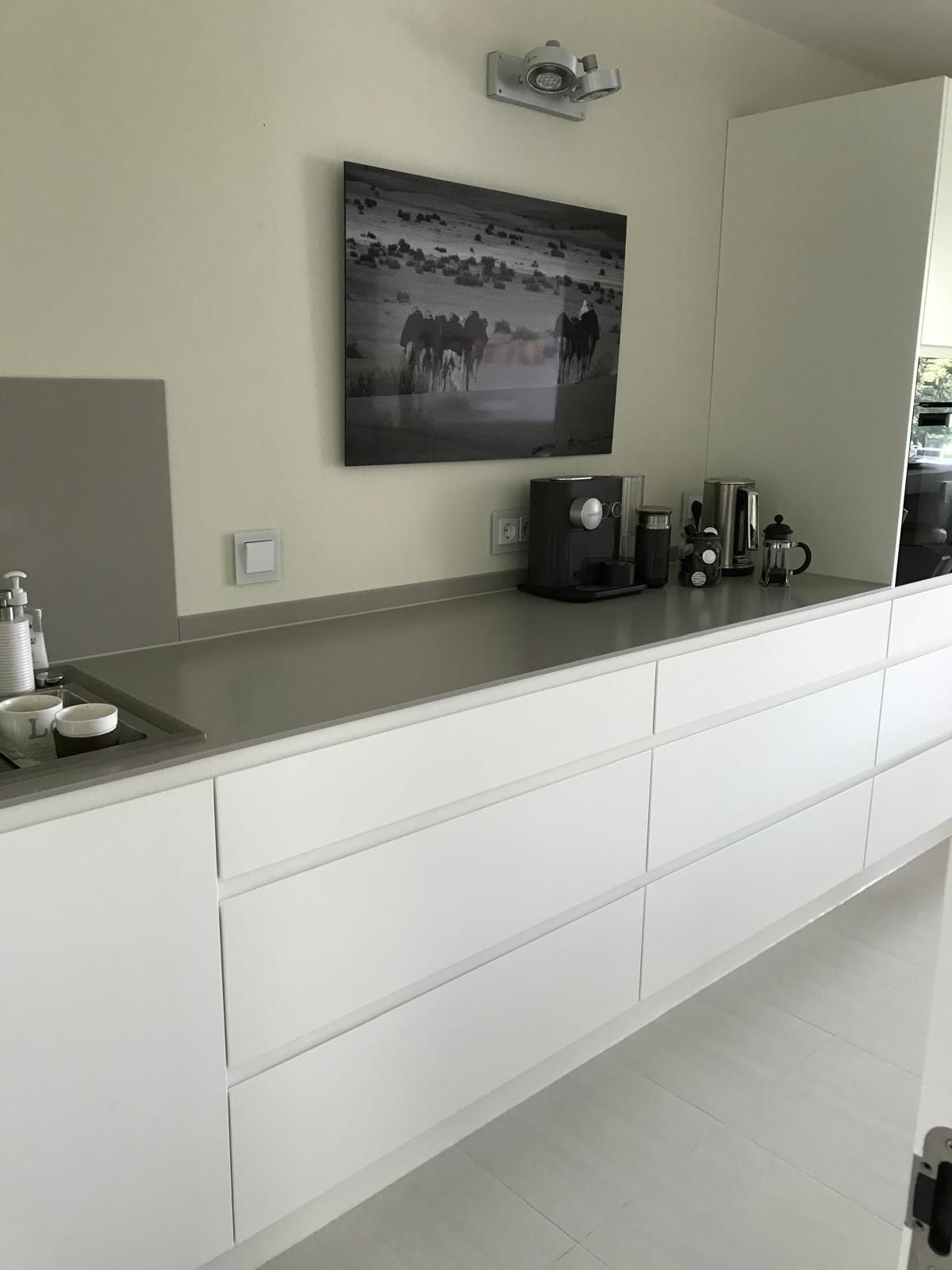 Eine Küche mit weißen Schränken und einem Bild an der Wand über der Theke