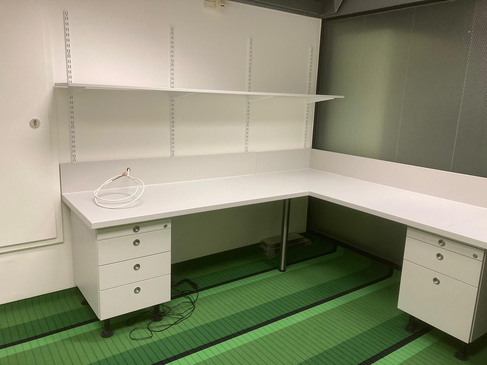Ein weißer Schreibtisch mit Schubladen und Regalen in einem Raum mit einem grünen Teppich.