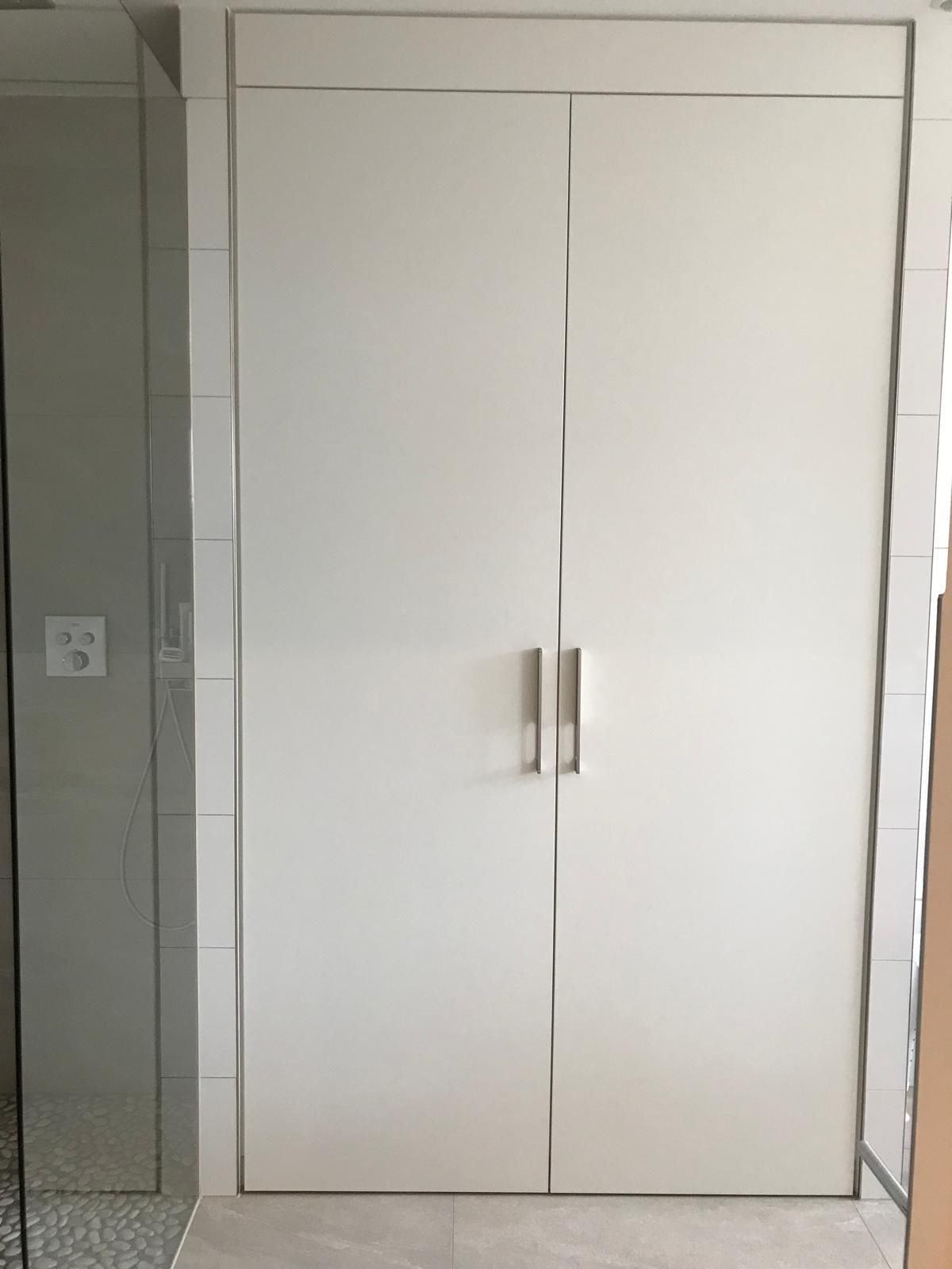 Ein weißer Schrank mit zwei Türen in einem Badezimmer.
