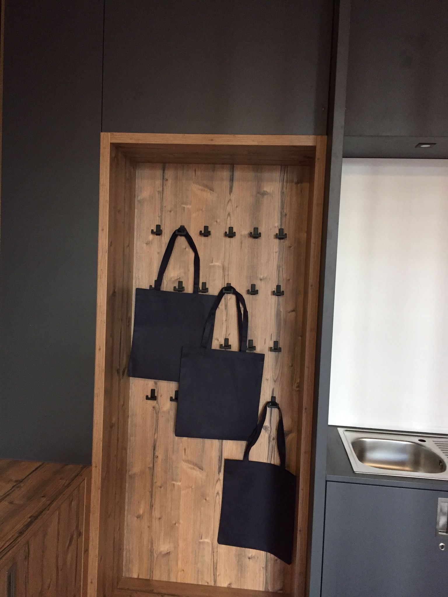 Drei schwarze Taschen hängen an Haken an einer Holzwand