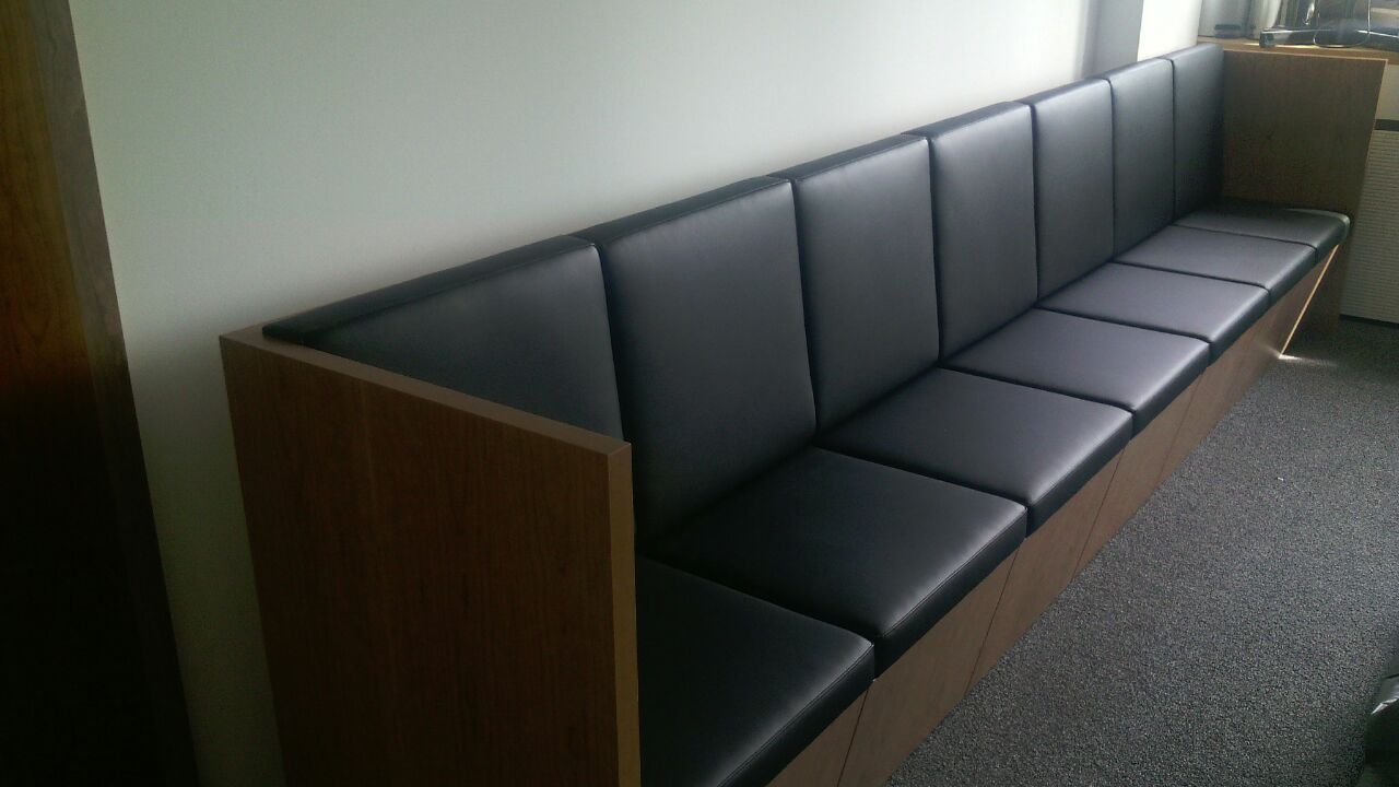 In einem Zimmer neben einem Fenster steht ein langes schwarzes Sofa.