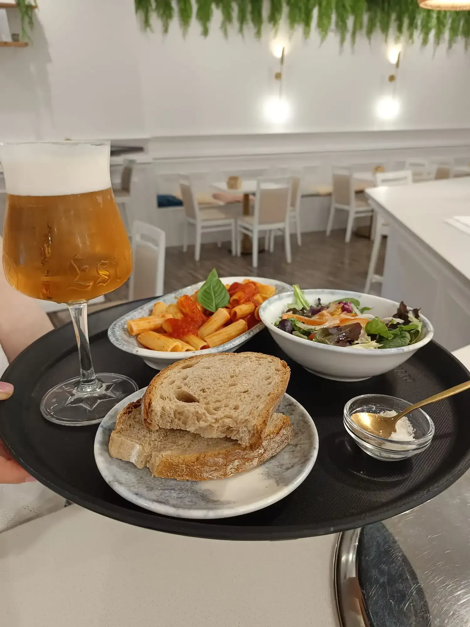 Cerveza y aperitivos en una bandeja sobre una mesa de café luminosa: cerveza, samosa, ensalada y tostadas.