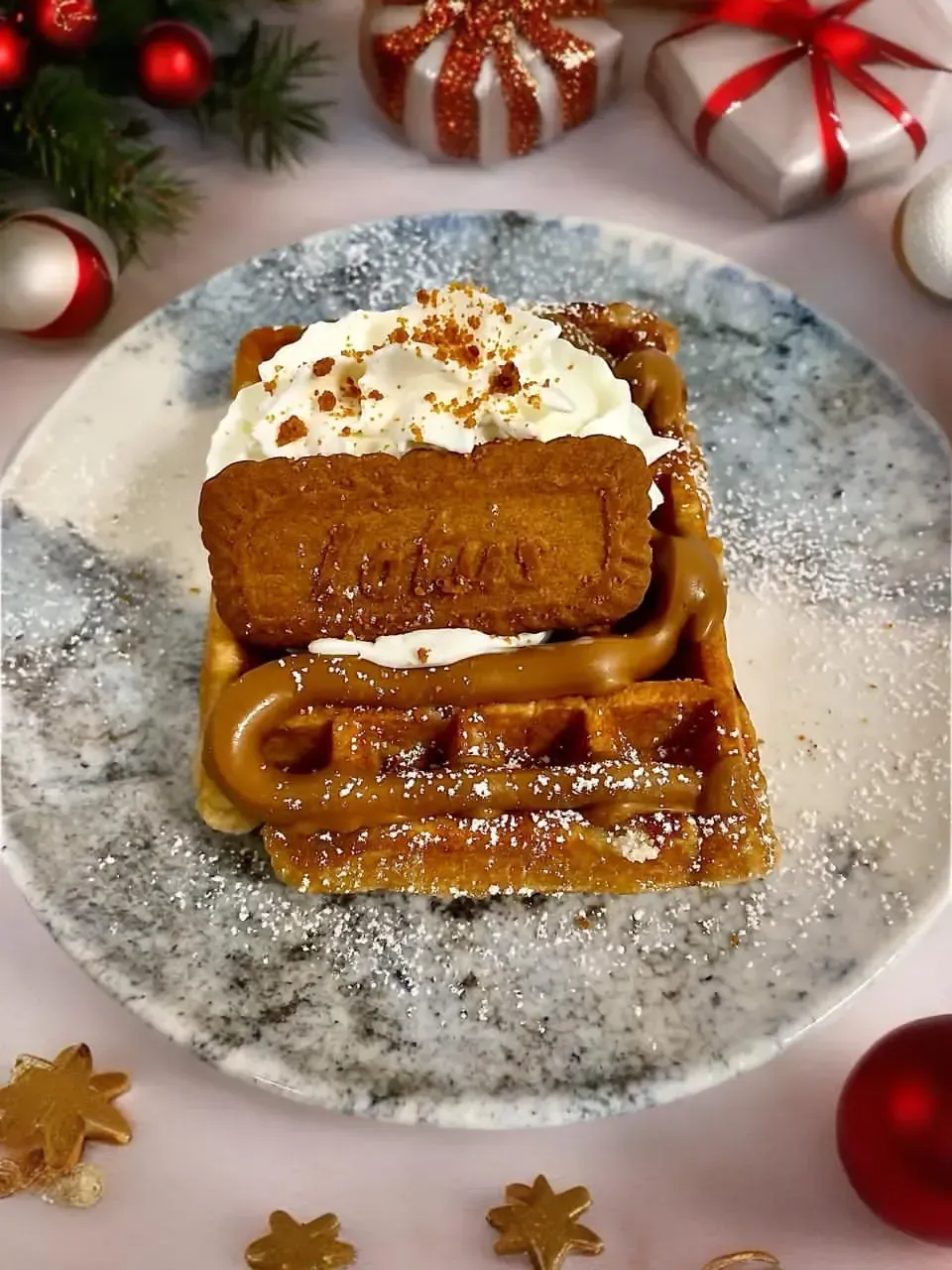 Una porción de postre de caramelo cubierta con crema batida en un plato, rodeada de decoraciones festivas navideñas.