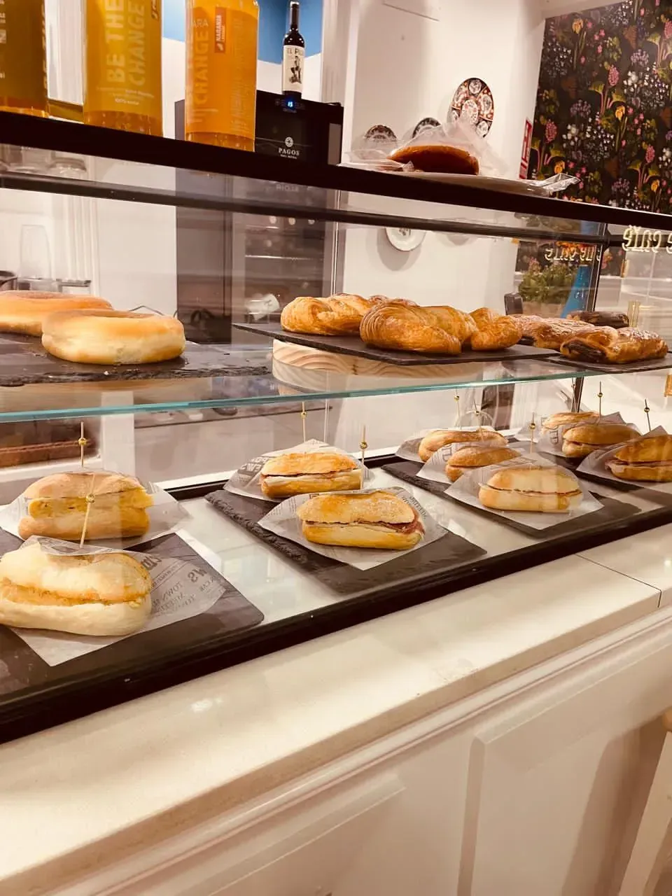 Vitrina de panadería con surtido de donas glaseadas y pasteles en estantes de vidrio.