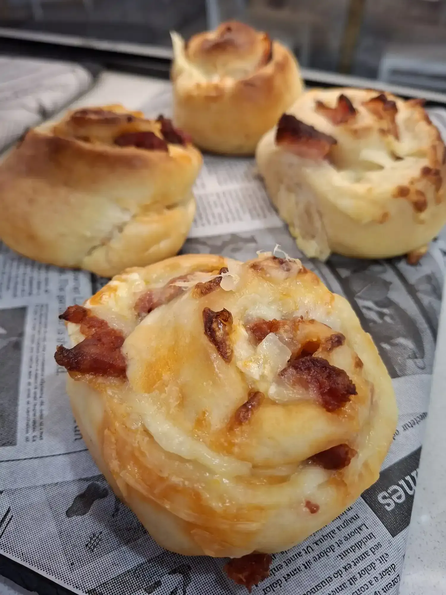 Cuatro rollos de canela horneados con la parte superior dorada sobre una bandeja forrada con papel de periódico.