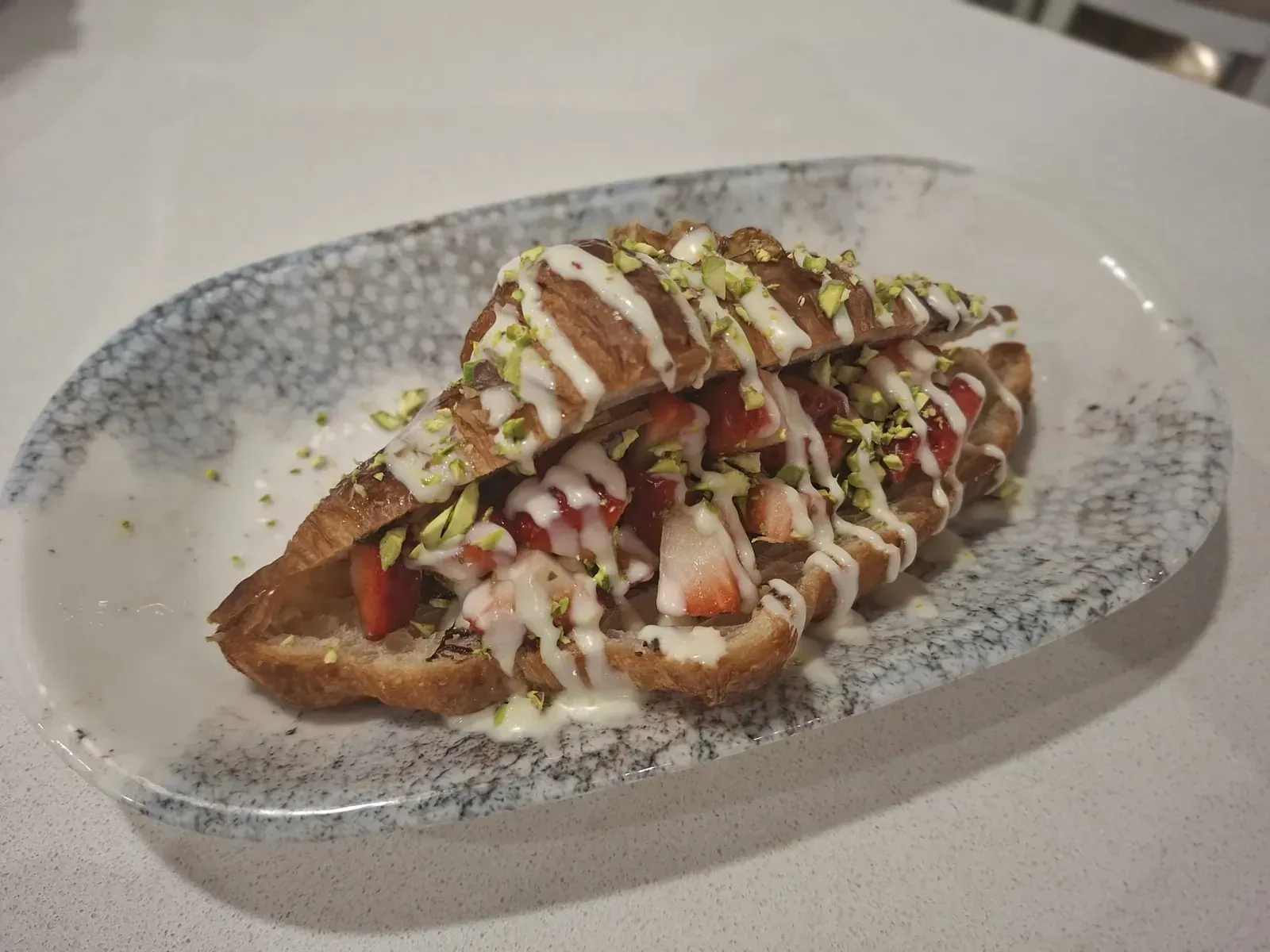 Sándwich a la parrilla cubierto con tomates picados y salsas, servido en un plato moteado.