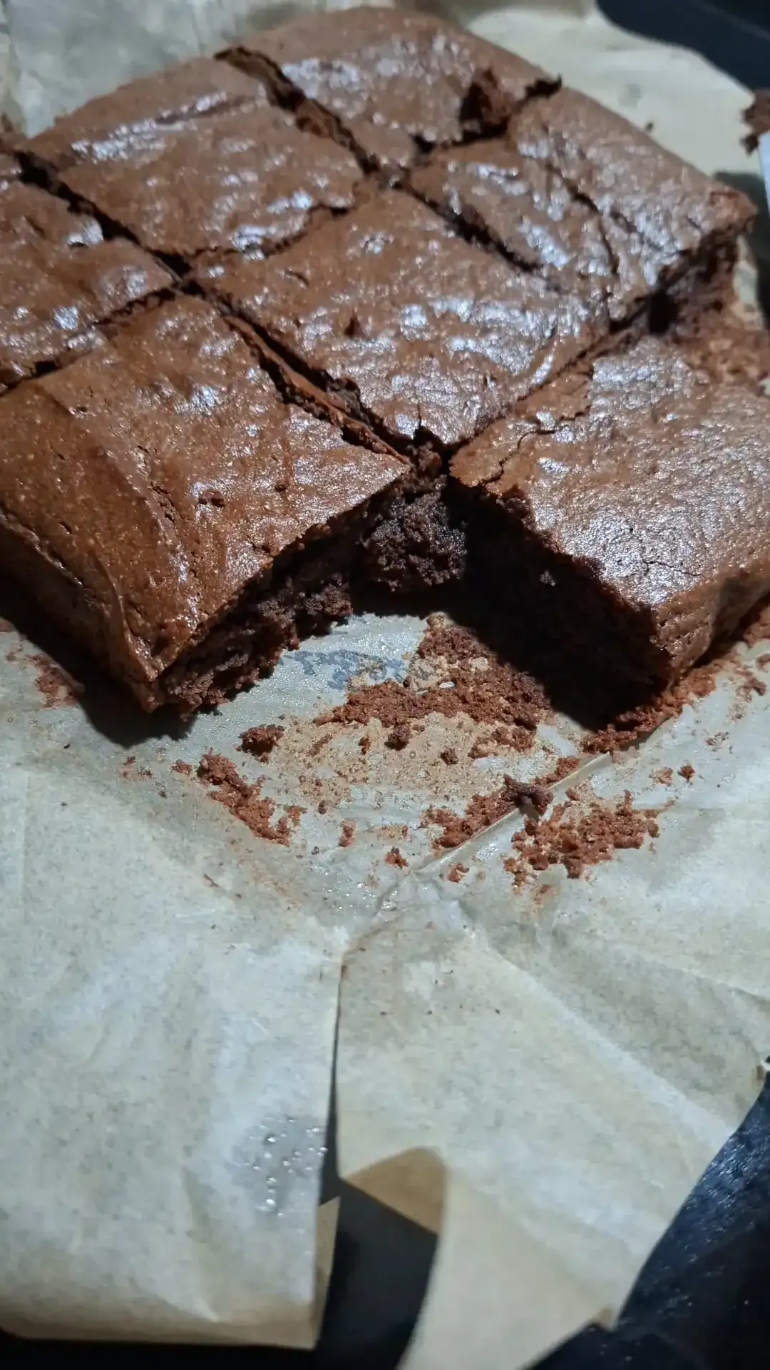 Brownies de chocolate sobre papel pergamino, cortados en cuadrados con un trozo faltante.