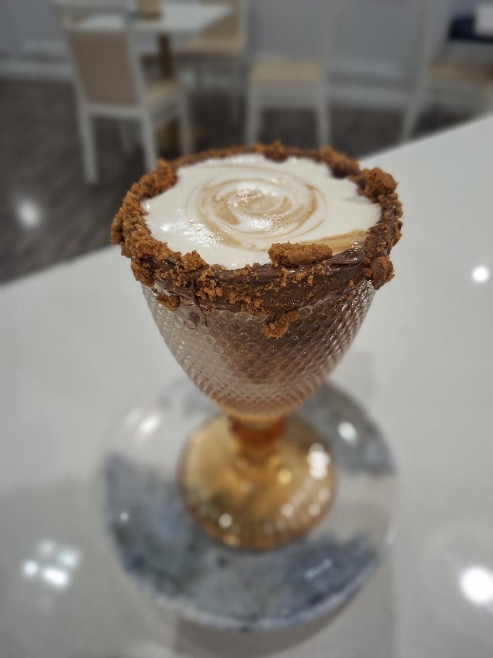 Latte Ferrato en una taza de cristal decorativa sobre un platillo, cubierto con migas de chocolate.