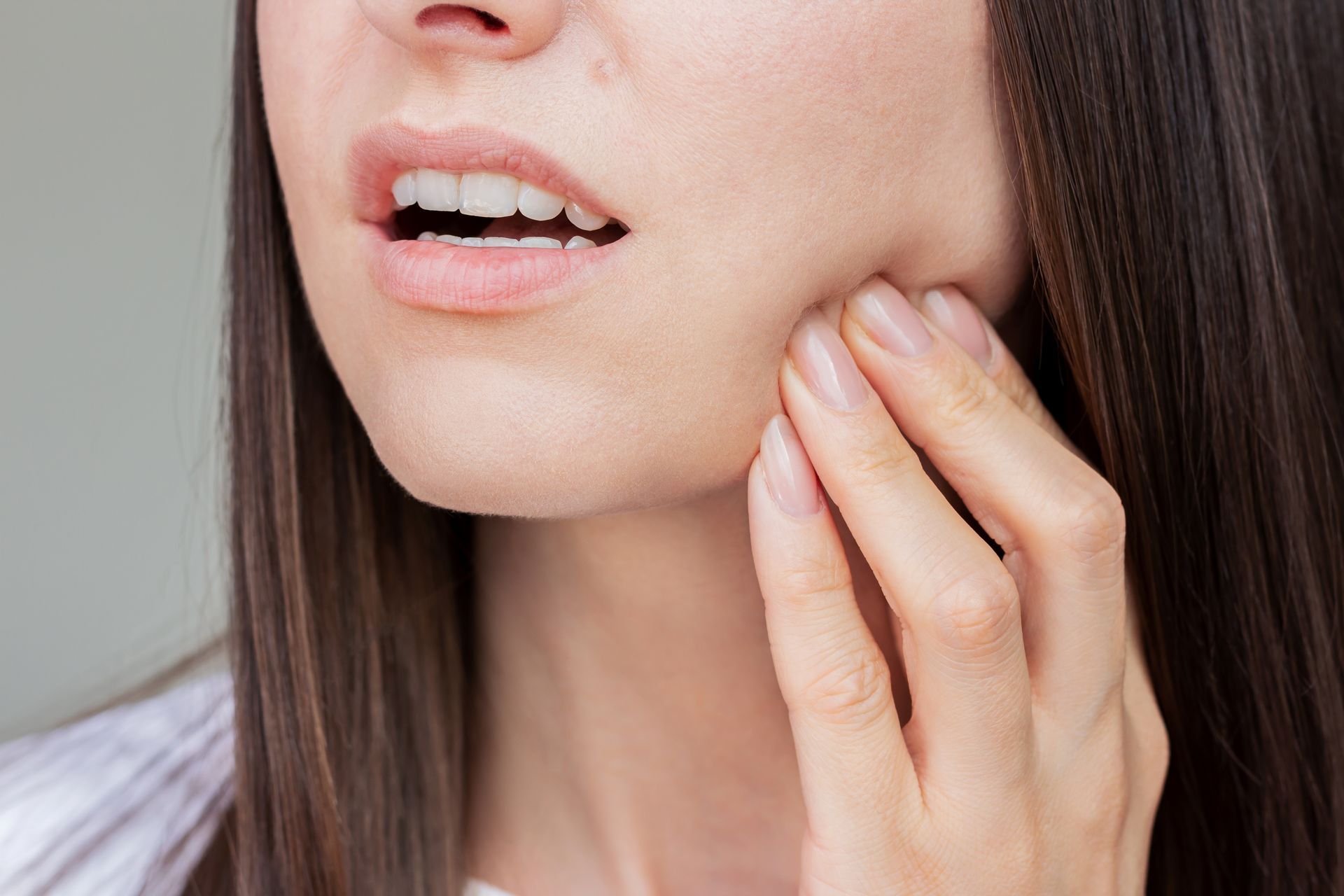 Frau hält Kiefer, möglicherweise mit Zahn- oder Kieferschmerzen.