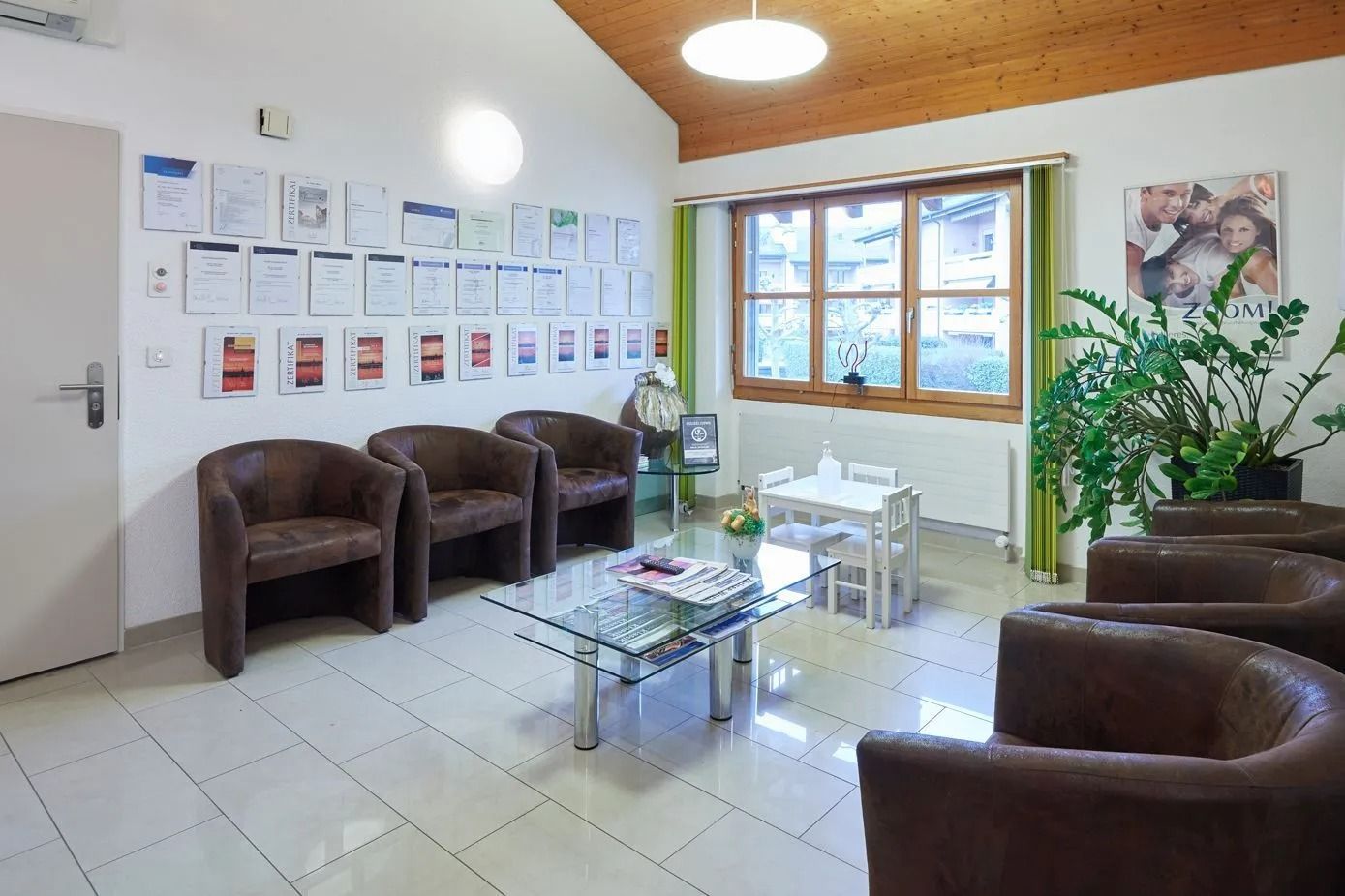 Wartezimmer mit braunen Lederstühlen, Glastisch und Diplomen an der Wand.