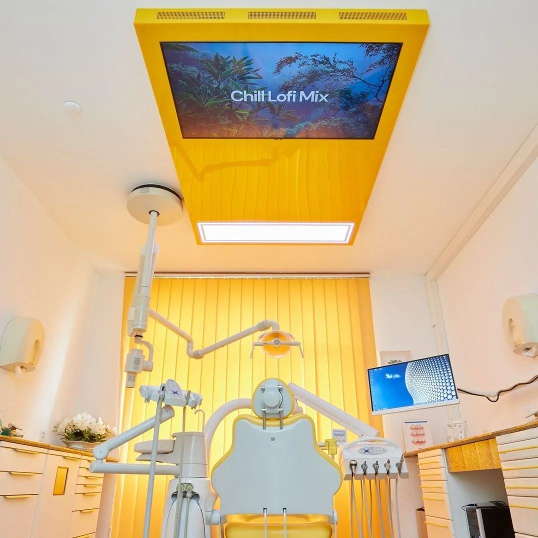 Gelbe Zahnarztpraxis, an der Decke montierter Bildschirm mit „ChillLoFi Mix“, Zahnarztstuhl und Ausrüstung.