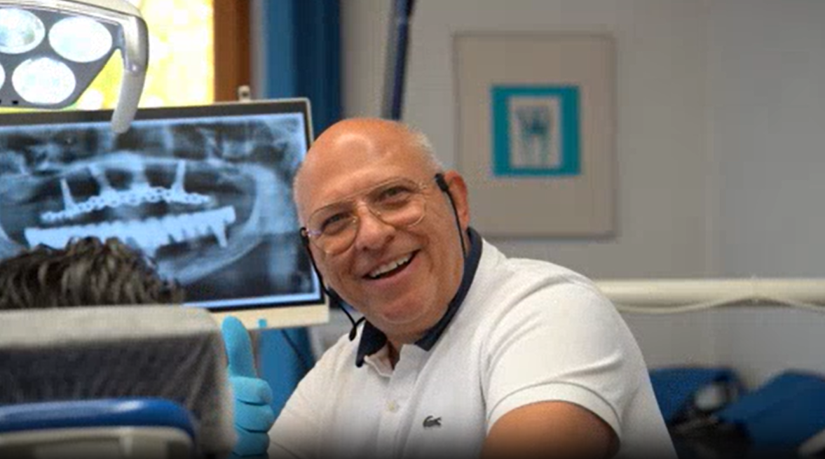 Zahnarztteam mit einem Zahnmaskottchen, alle zeigen den Daumen nach oben. Helle Büroumgebung.