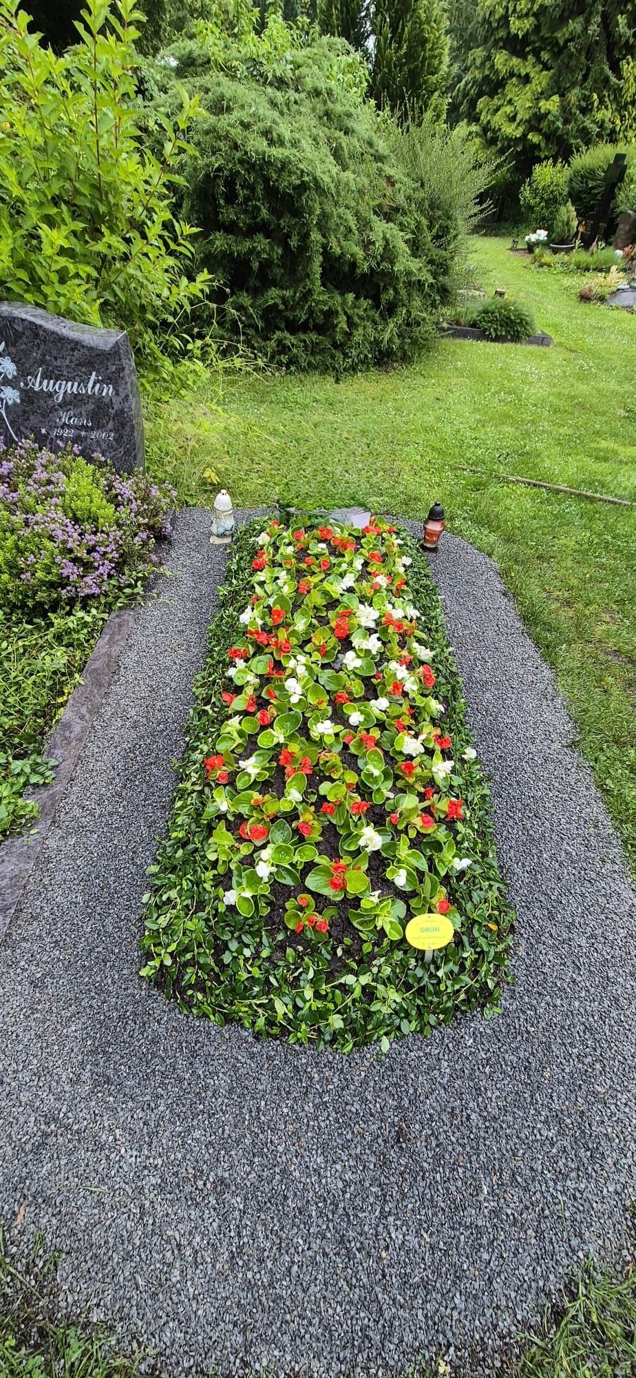 Ein mit Steinen eingefasstes Blumenbeet mit farbenprächtigen Blüten auf einem Friedhof