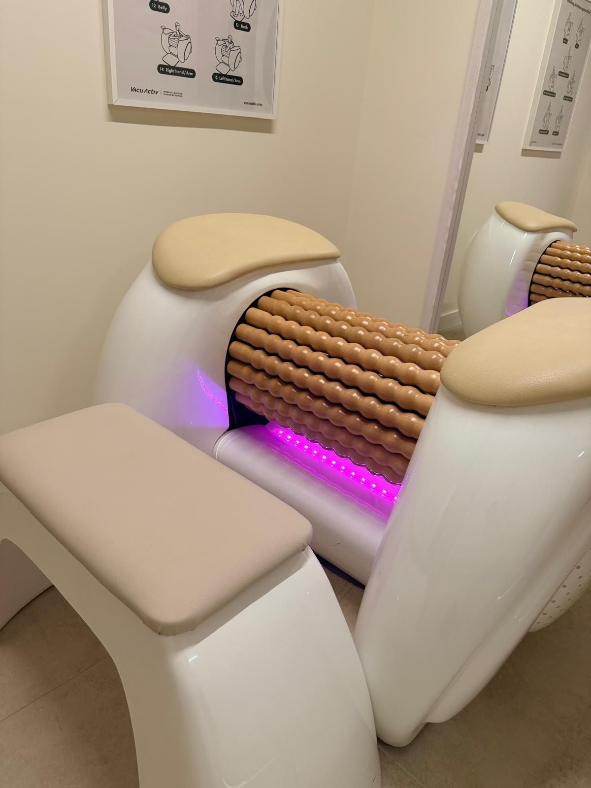 Una máquina de masaje con un tambor cilíndrico de rodillos con textura de madera, reposabrazos acolchados de color beige