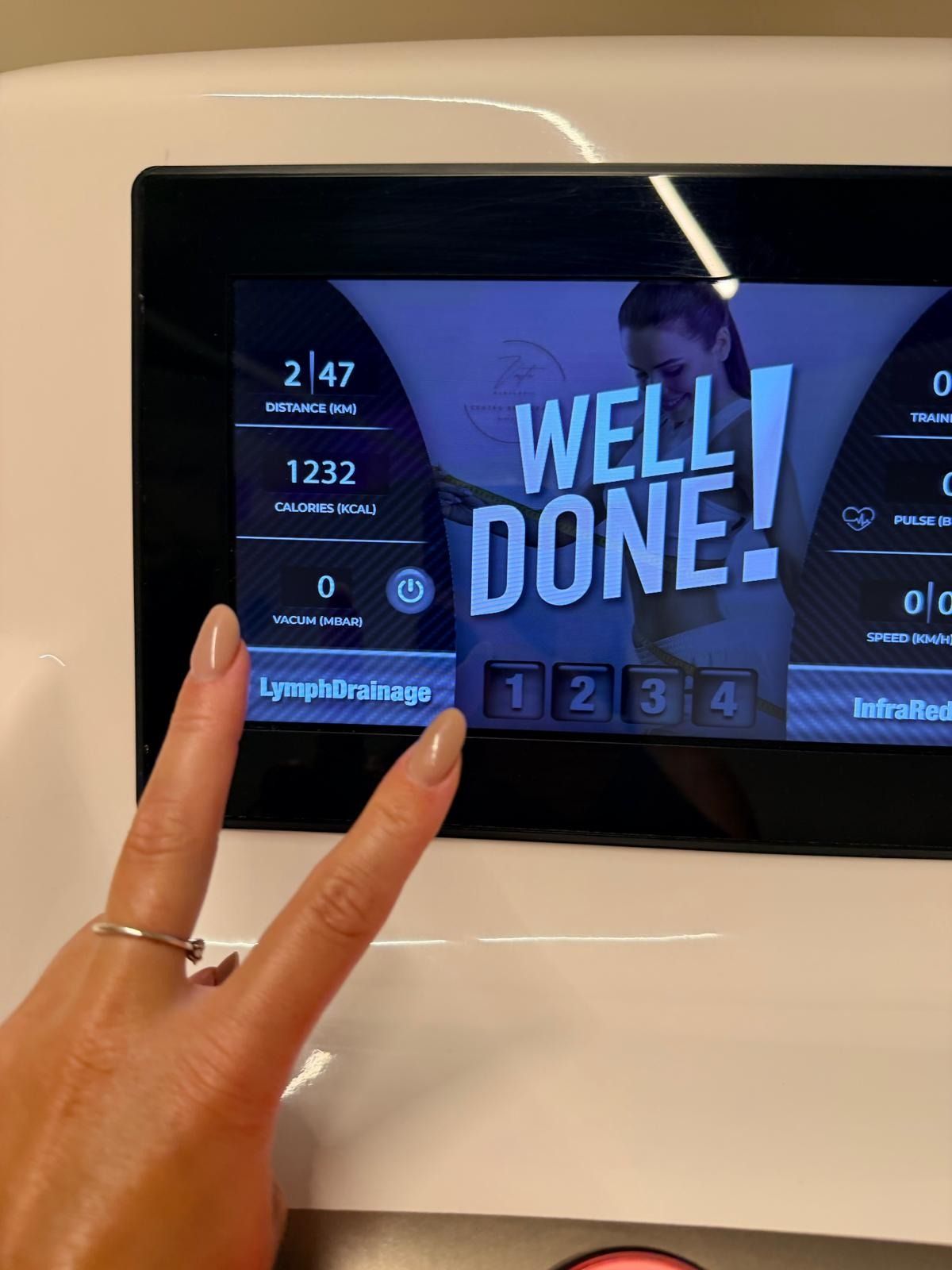 Una persona hace el signo de la paz frente a la pantalla de una máquina de ejercicios que muestra 