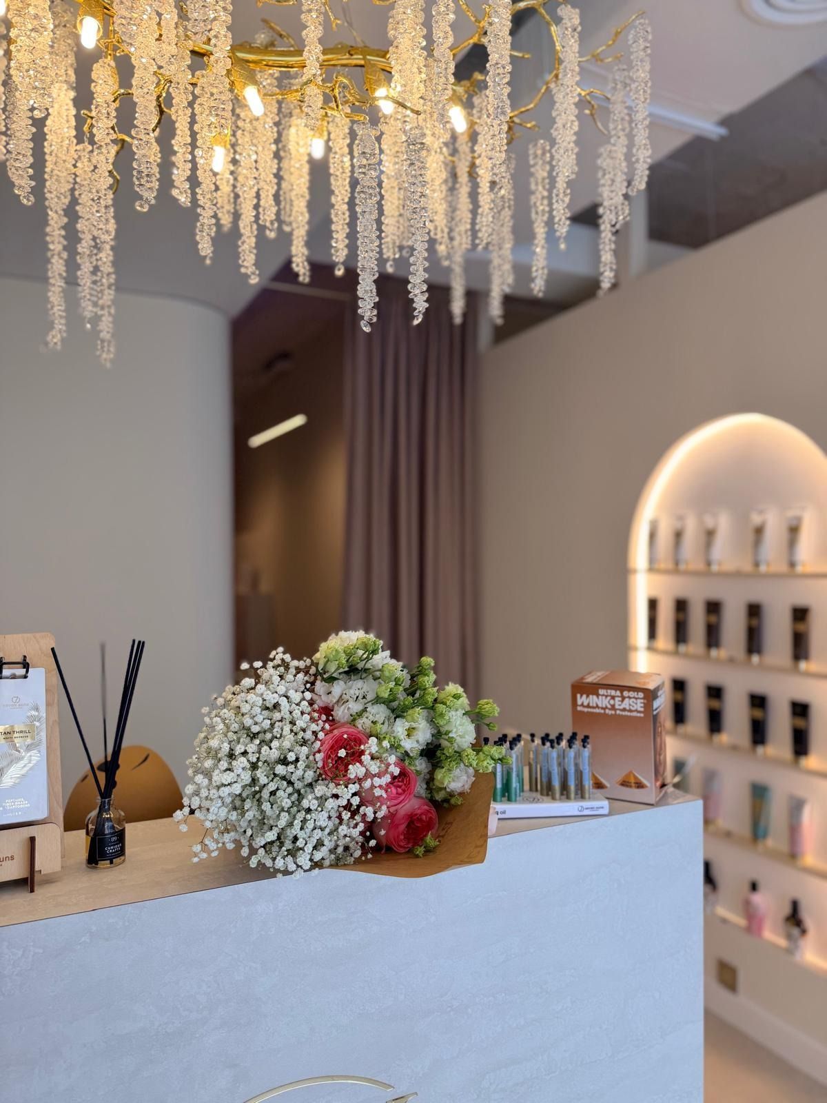 Un ramo de flores reposa sobre un moderno mostrador de recepción en una boutique, bajo una lámpara de araña de cristal