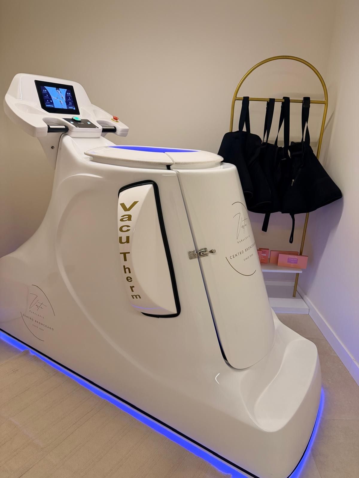 Una máquina de fitness VacuTherm blanca con iluminación inferior azul junto a un perchero