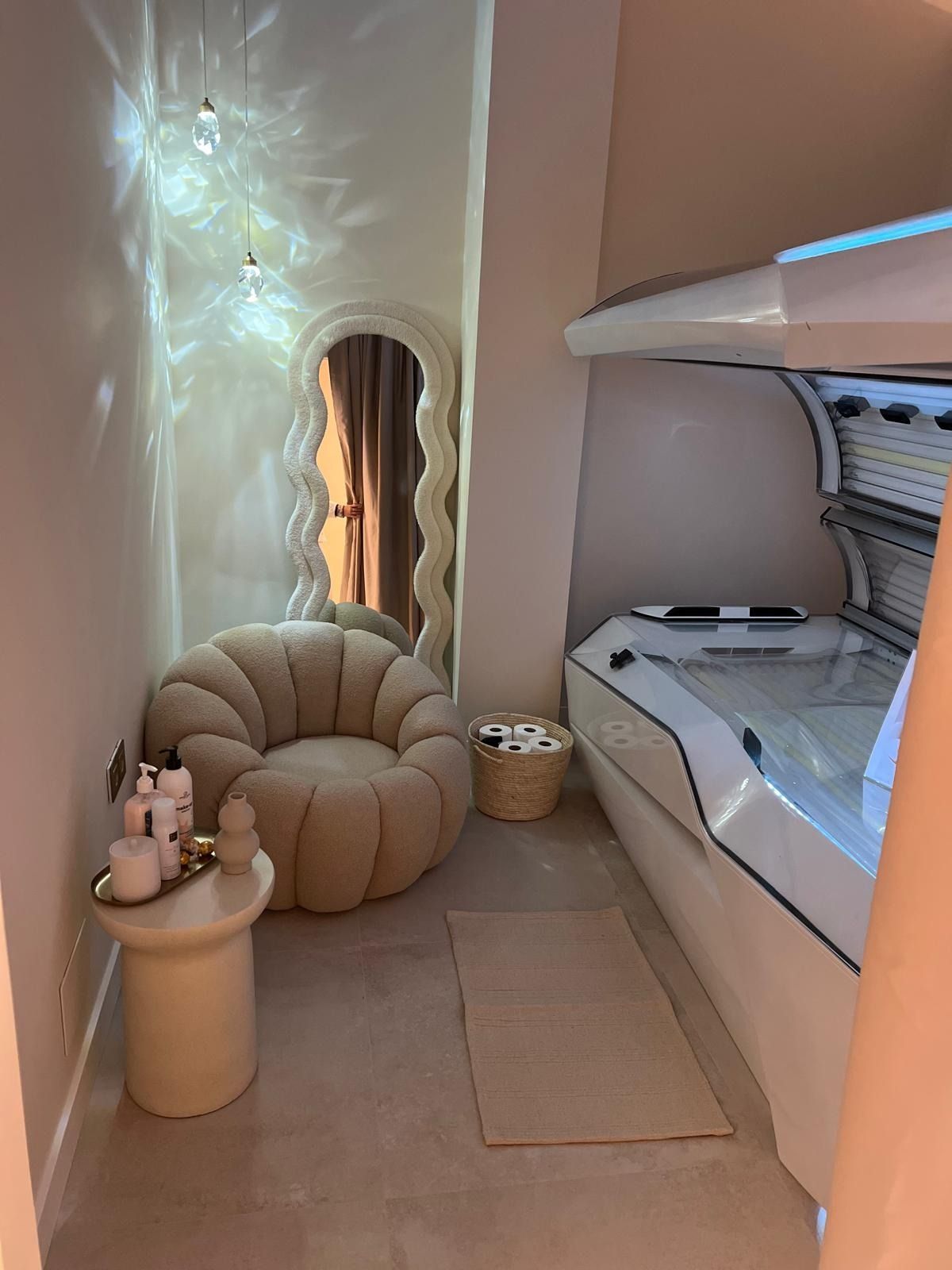 Una cabina de bronceado moderna y minimalista cuenta con una gran silla circular de color beige, un espejo de pie ondulado