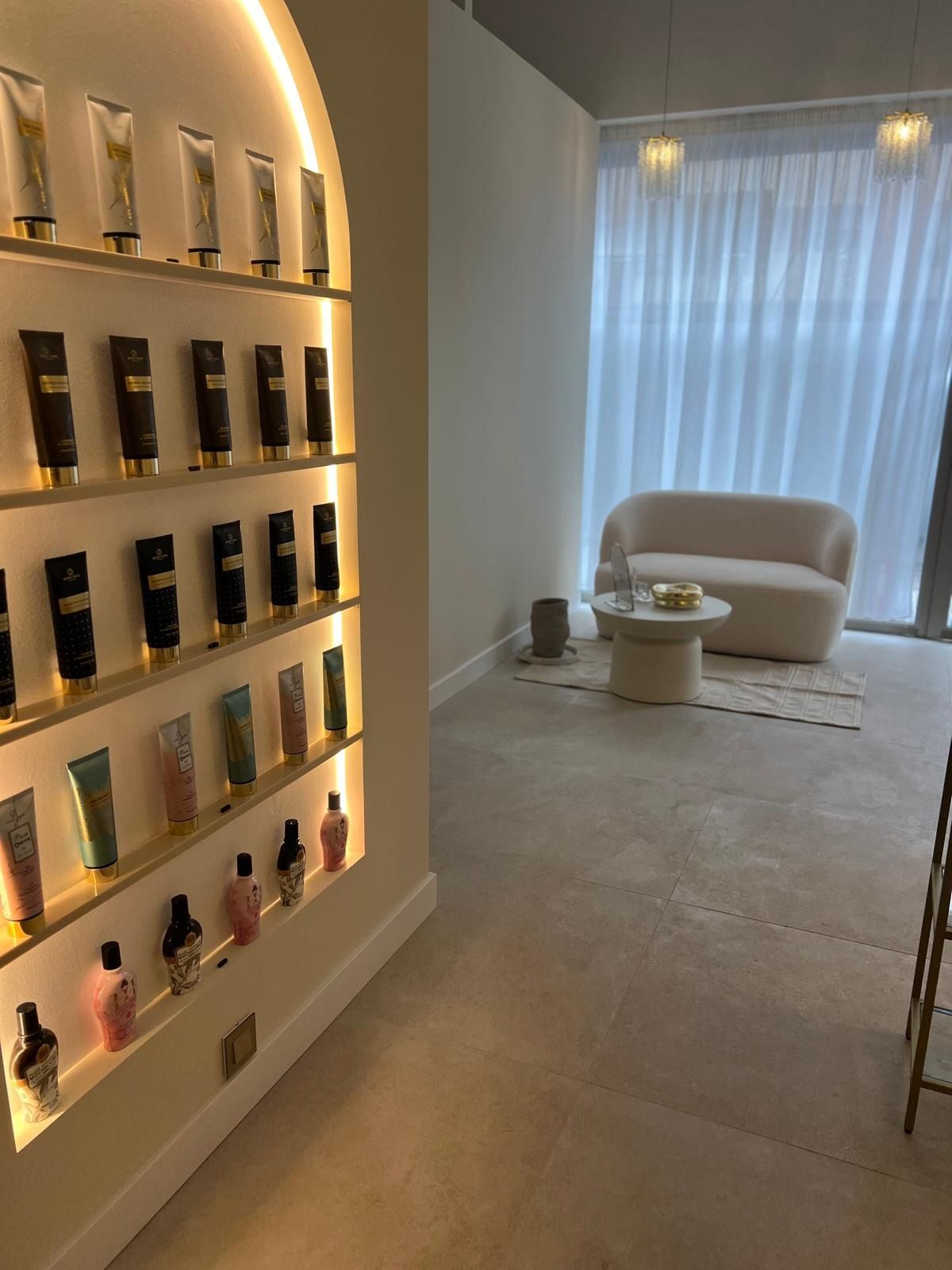 Un interior de salón minimalista con una estantería arqueada iluminada que exhibe productos para el cuidado de la piel