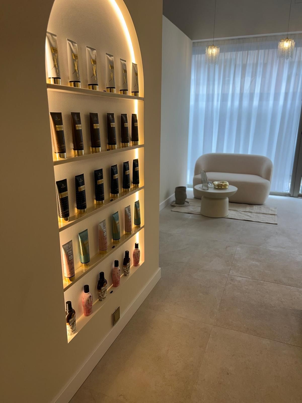 Un expositor de productos para el cuidado de la piel colocado en una pared arqueada, en una habitación de color crema