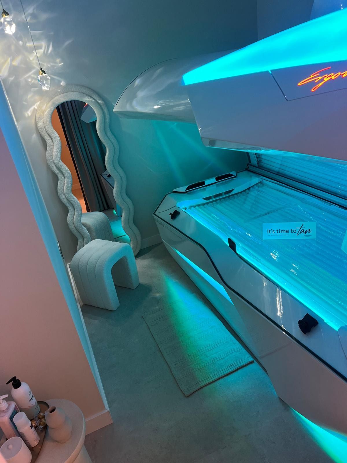 Una habitación moderna con una cama de bronceado que emite una luz azul, un espejo de pie ondulado