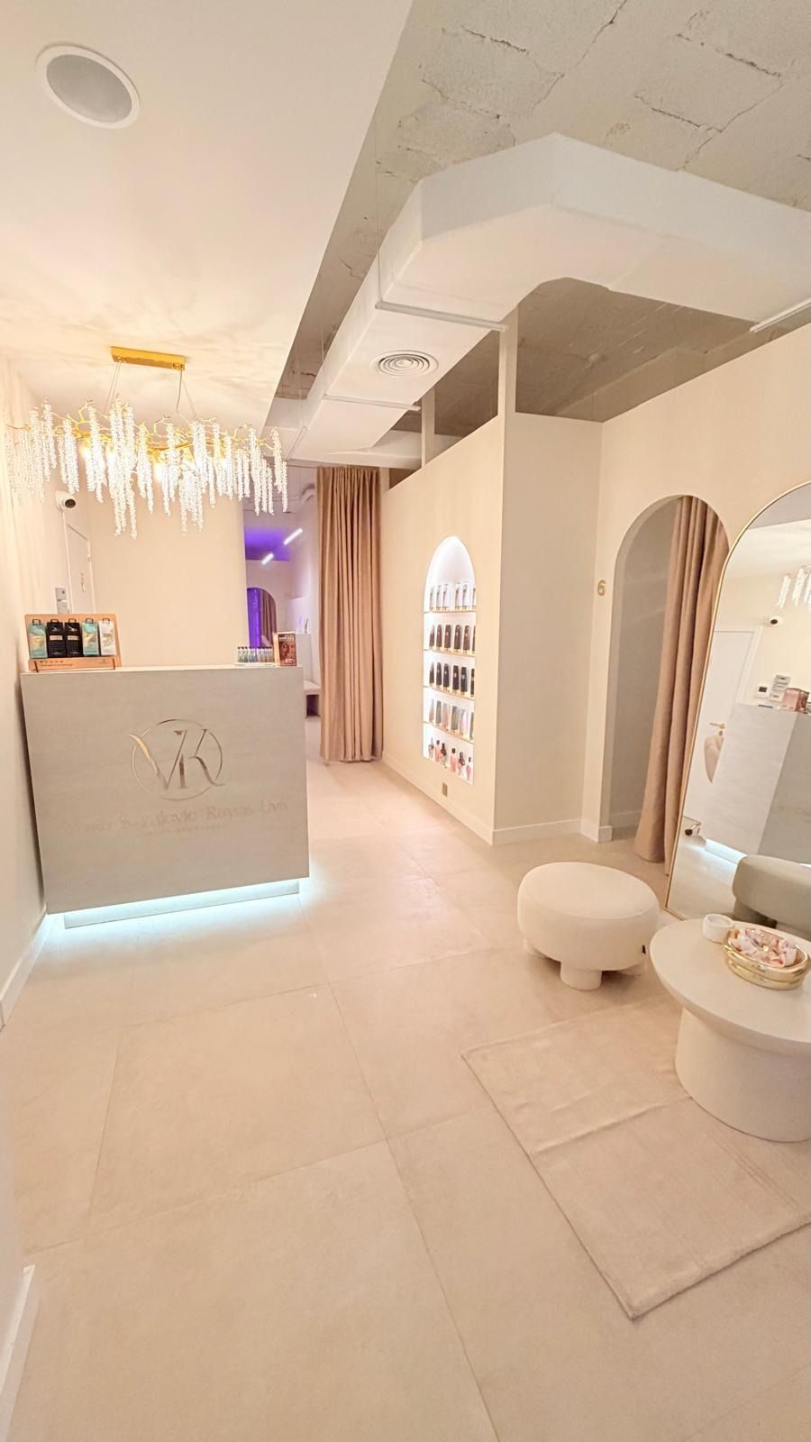 Una elegante y minimalista zona de recepción en tonos beige neutros, con una lámpara de araña sofisticada y un mostrador