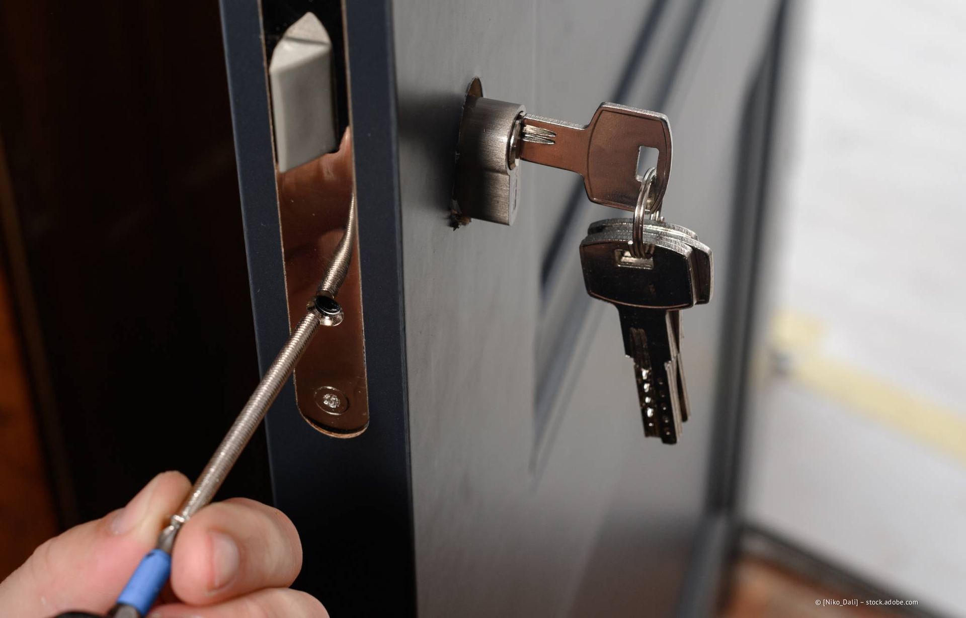 Hand mit Schraubendreher zum Einstellen des Türschlosses, Schlüssel im Schloss.