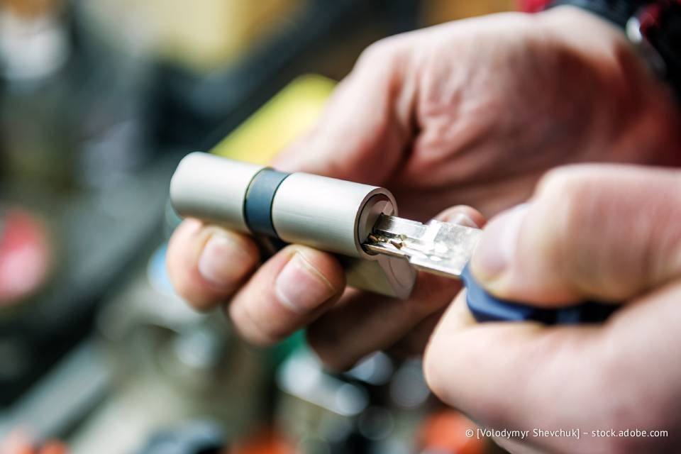 Hände stecken einen Schlüssel in einen silbernen Türschlosszylinder.