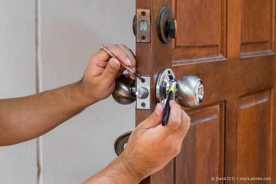 Person, die mit einem Schraubenzieher einen Türknauf an einer Holztür befestigt.