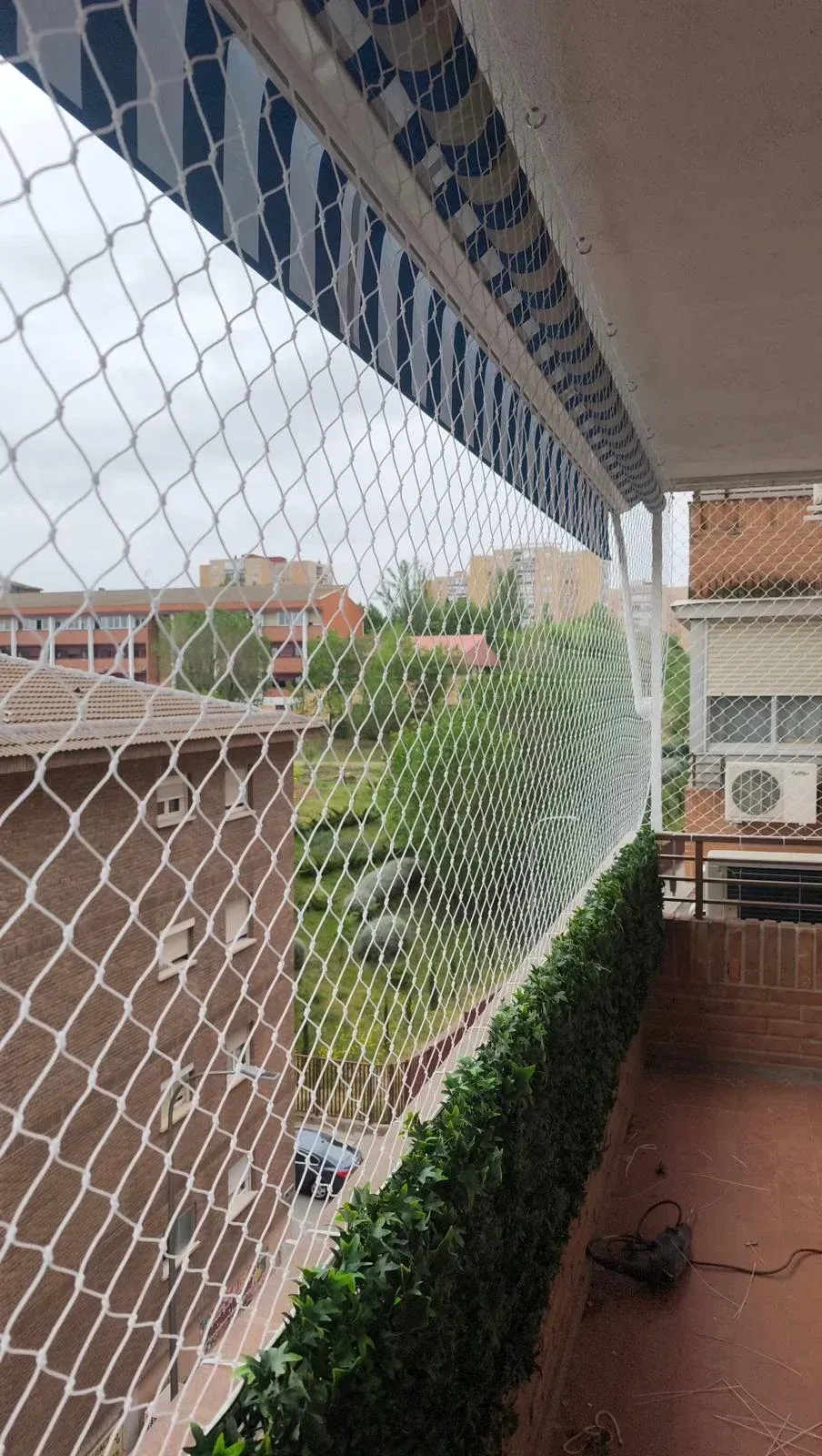 Balcón con red de seguridad blanca con vistas a los tejados cercanos y a un pequeño jardín en la planta baja.