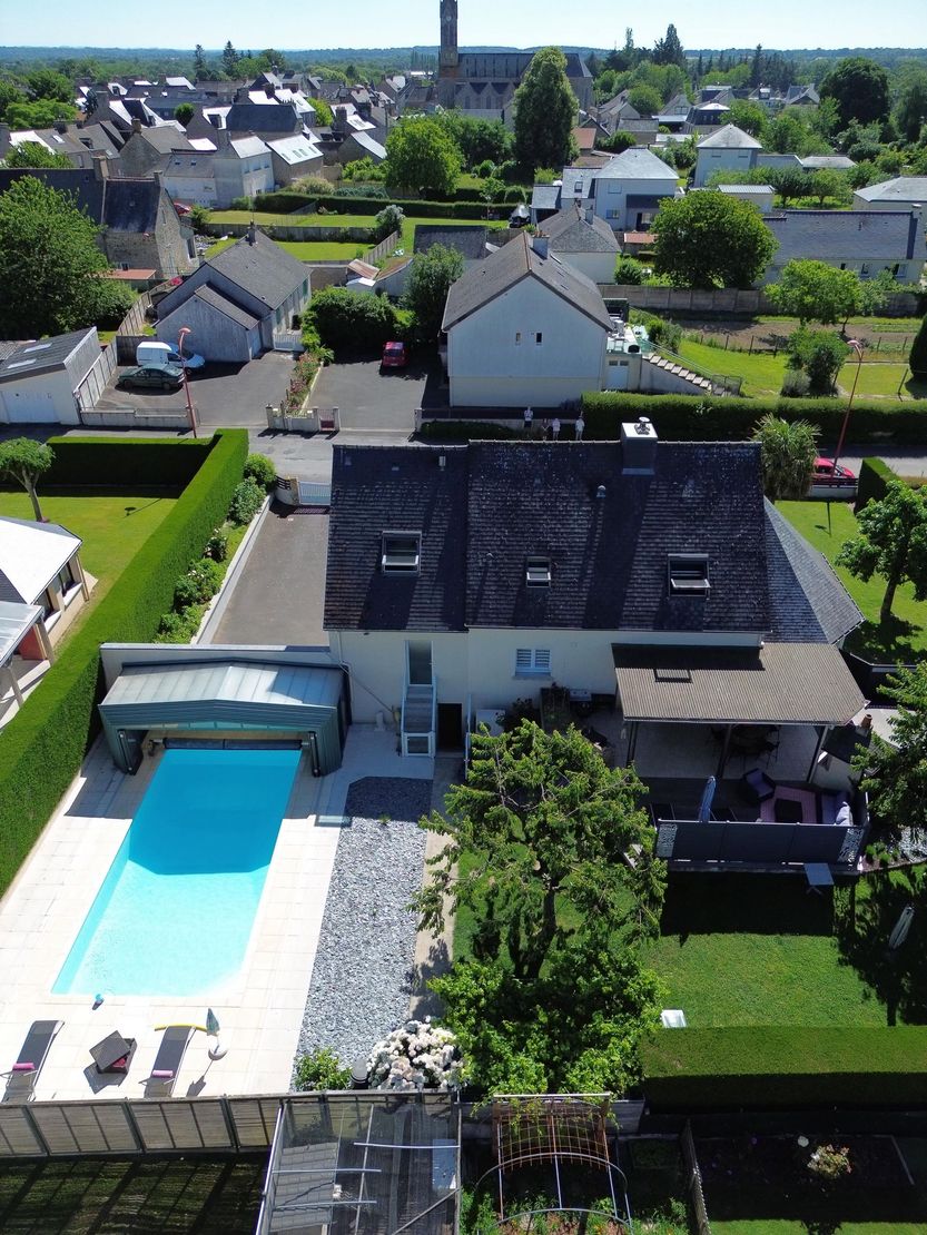 Vue aérienne d'une maison de banlieue avec piscine dans le jardin et maisons voisines.