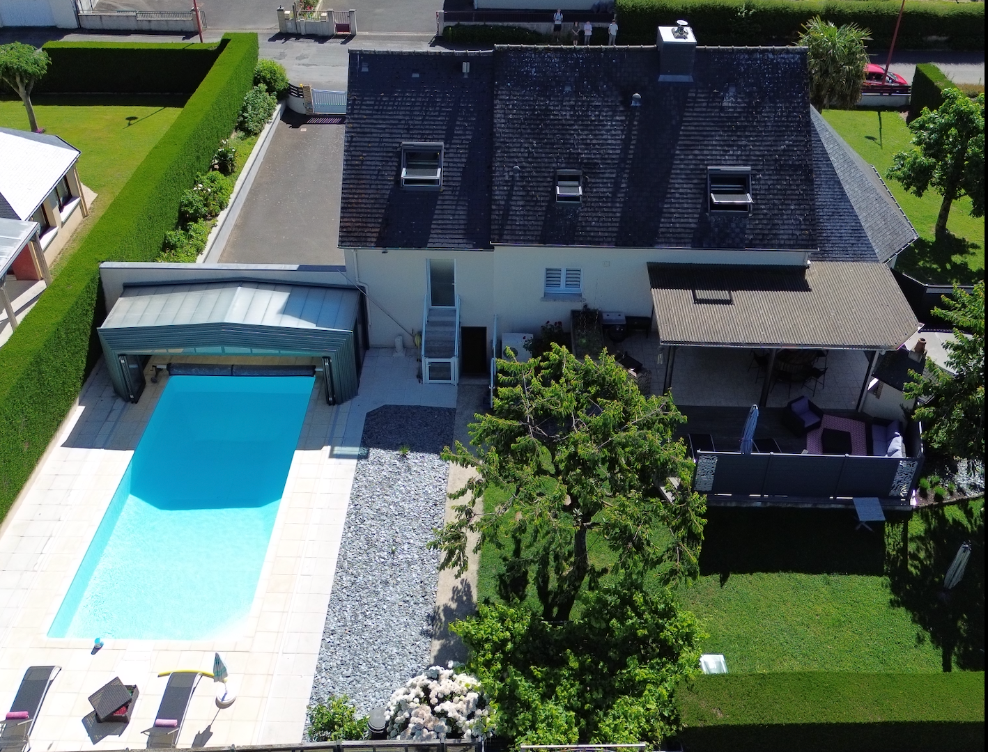Maison jaune moderne avec toit en ardoise, grande pelouse et parterre de fleurs colorées à côté d'un grand palmier