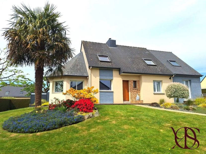 Maison moderne avec toit en pente, murs jaunes et jardin coloré à l'avant par une journée ensoleillée