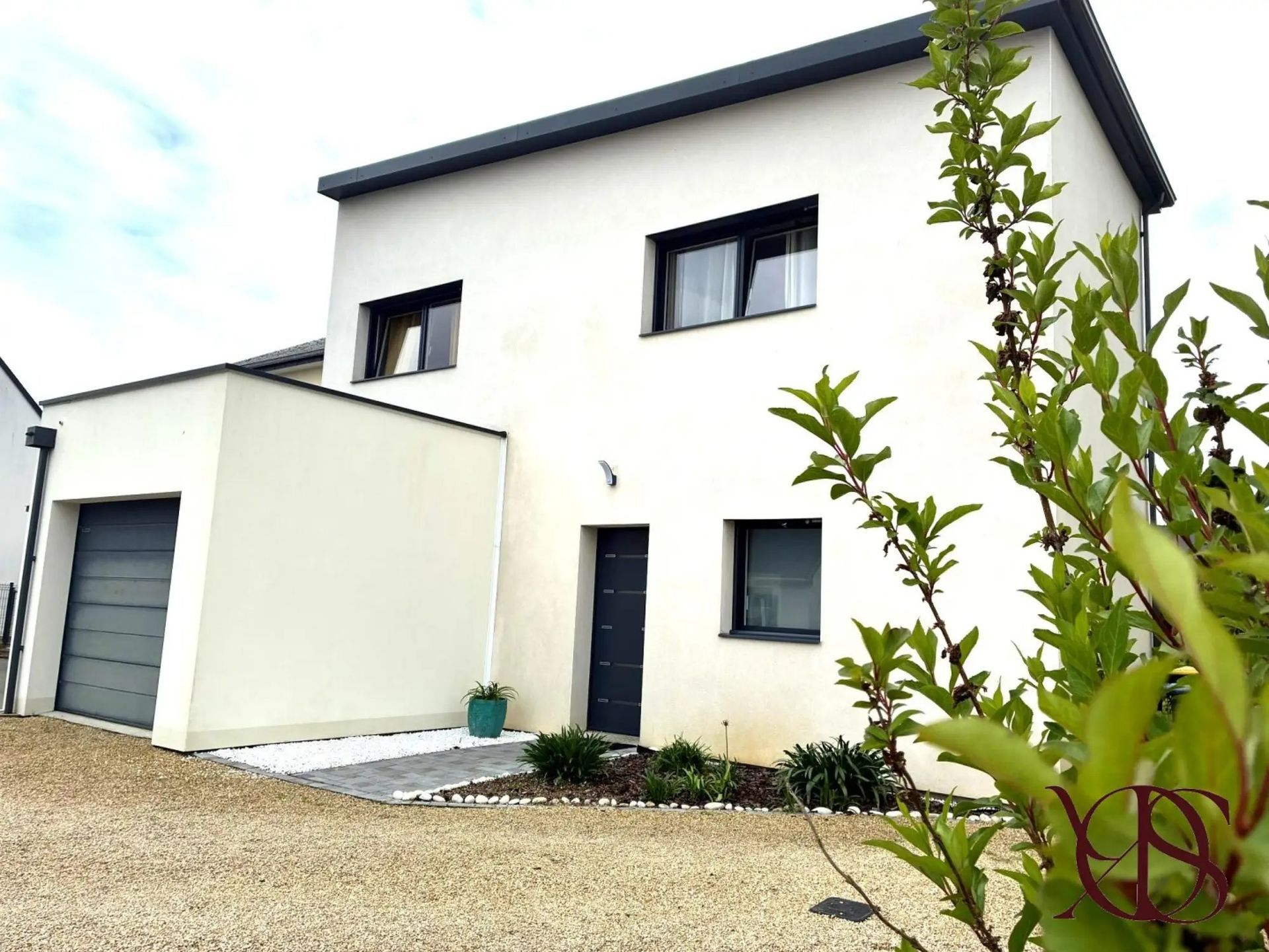Maison moderne blanche de deux étages avec garage et petit jardin à l'avant sous un ciel nuageux