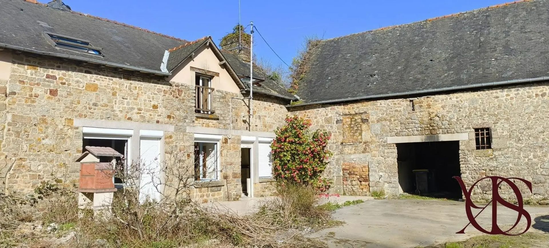 Cour d'une vieille ferme en pierre avec une porte blanche, une grange sombre et un ciel bleu