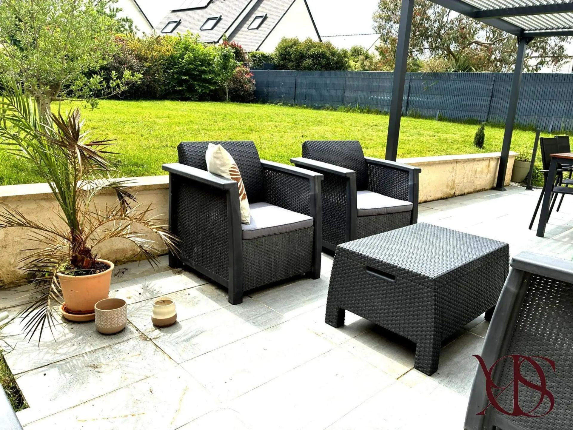 Patio avec chaises noires, table, plante en pot et pelouse verte, avec une pergola.