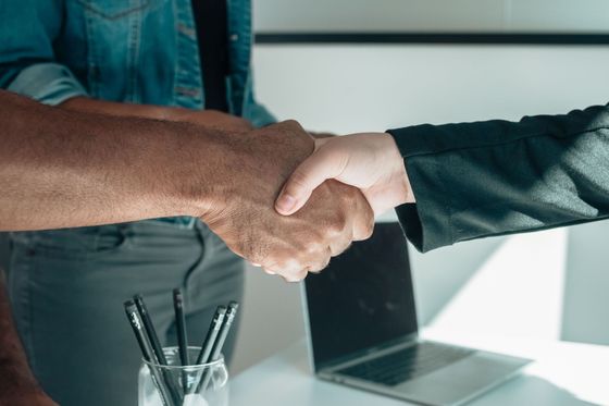 Deux personnes se serrent la main de l'autre côté d'un bureau, un ordinateur portable en arrière-plan.