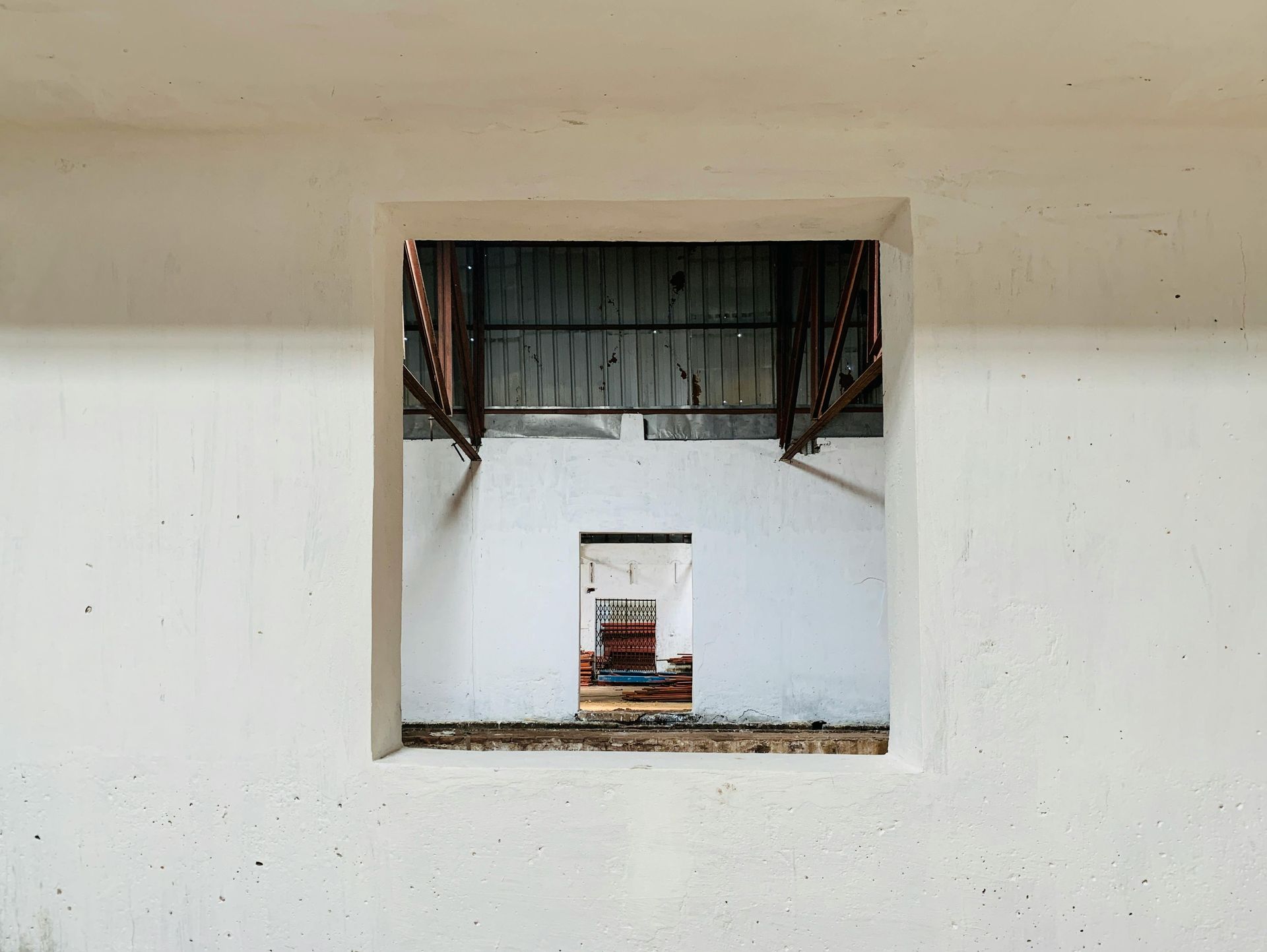 Un mur blanc percé d'une ouverture carrée encadrant un intérieur industriel sombre et lointain, ainsi qu'une autre porte.