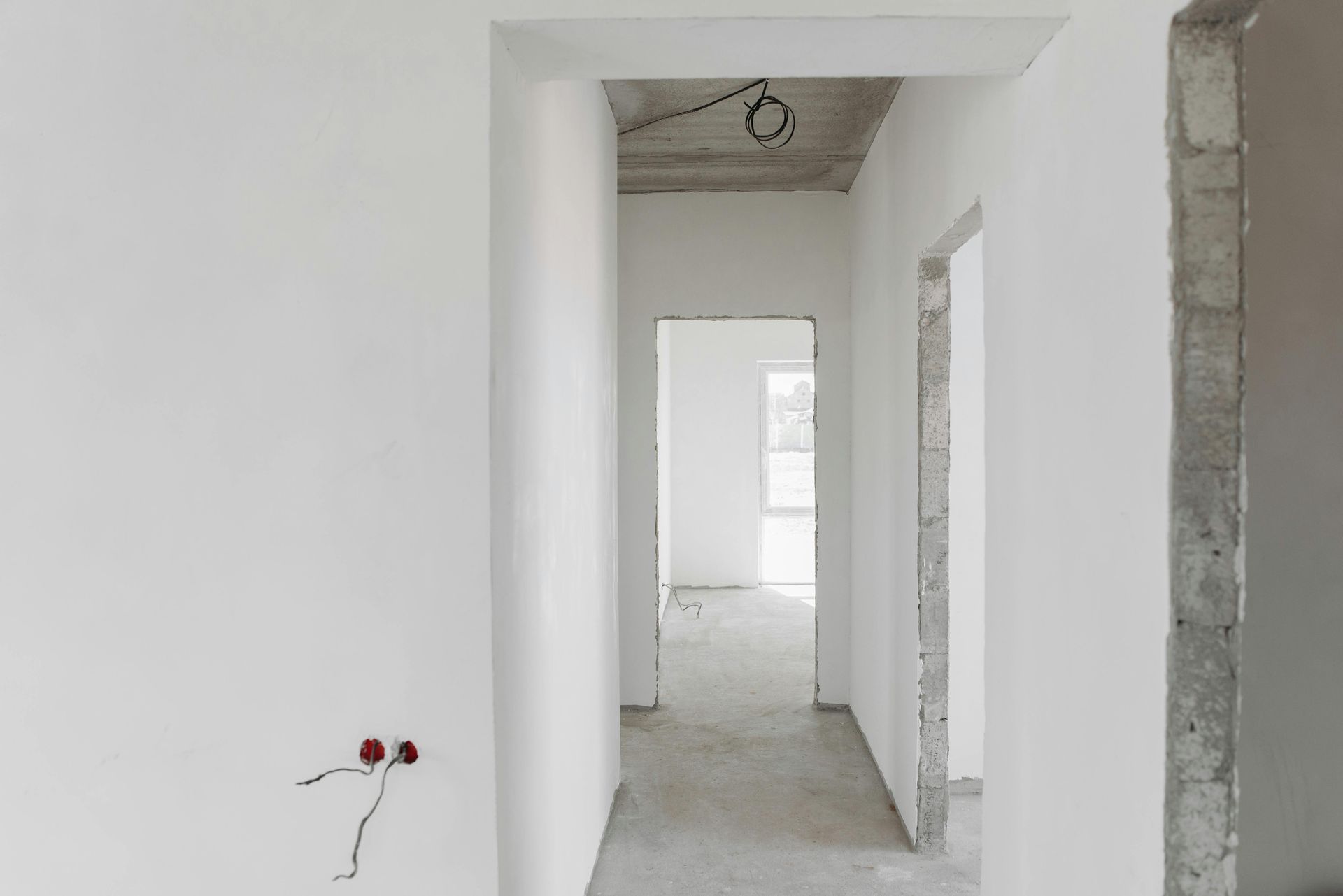 Couloir blanc inachevé avec portes, câbles électriques apparents et sol en béton.