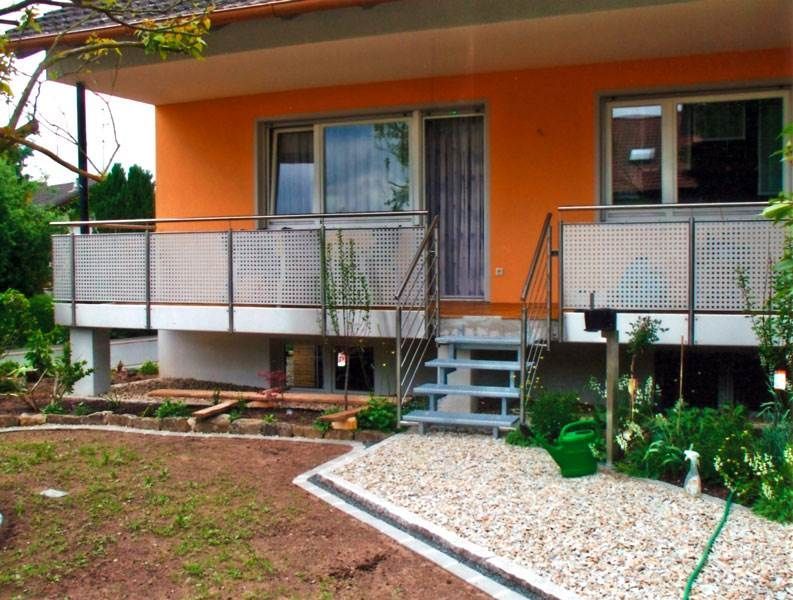 Orangefarbenes Haus mit Balkon, Metallgeländer und Stufen zu einem Kieselweg im Garten.