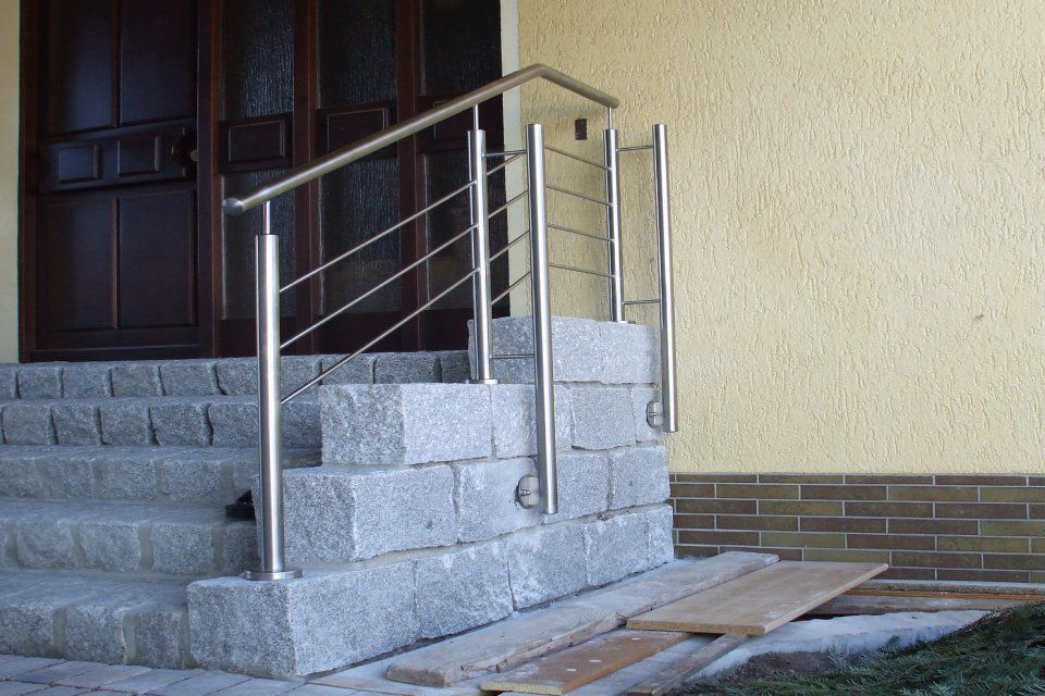 Edelstahlgeländer an Granitstufen, die zu einer Tür führen; gelbe Außenwand.